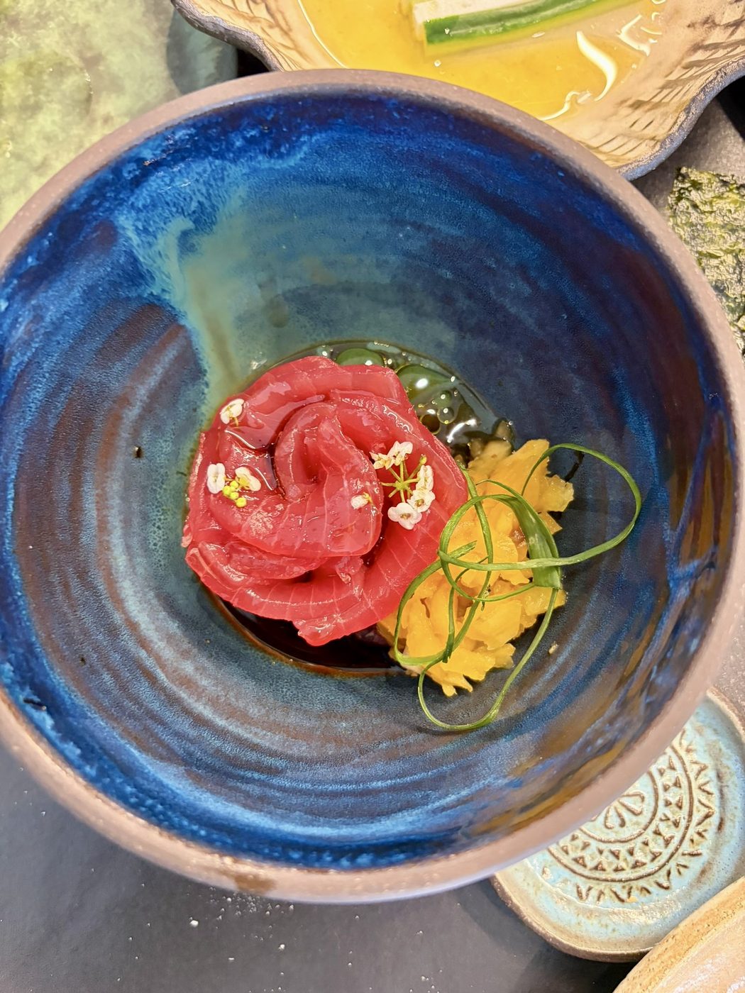 Maguro sliced thin and coiled into a rose in a deep blue bowl, with dark soy and small white flowers